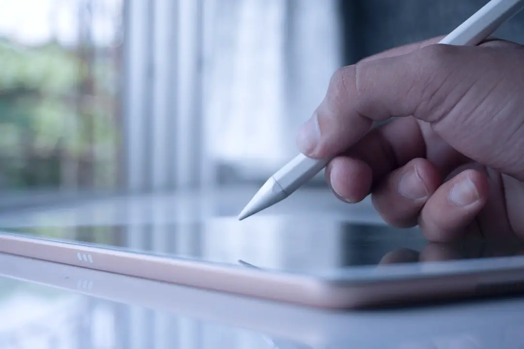 a person holding a pen and writing on a tablet